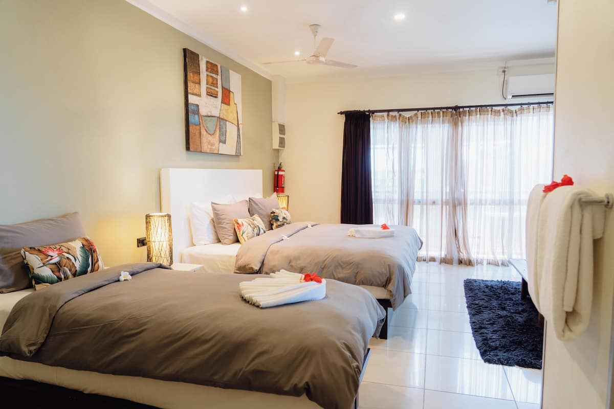 Habitación de hotel con dos camas, ventilador de techo, ventana grande con cortinas y un cuadro en la pared.