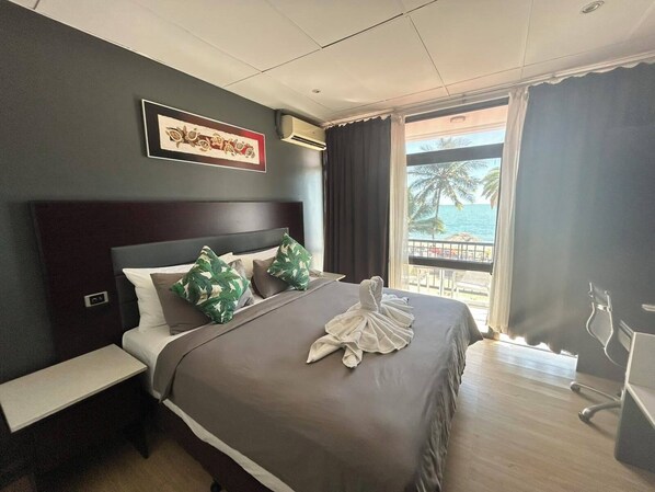 Habitación de hotel con una cama grande, una mesita de noche, una silla y vista al océano.