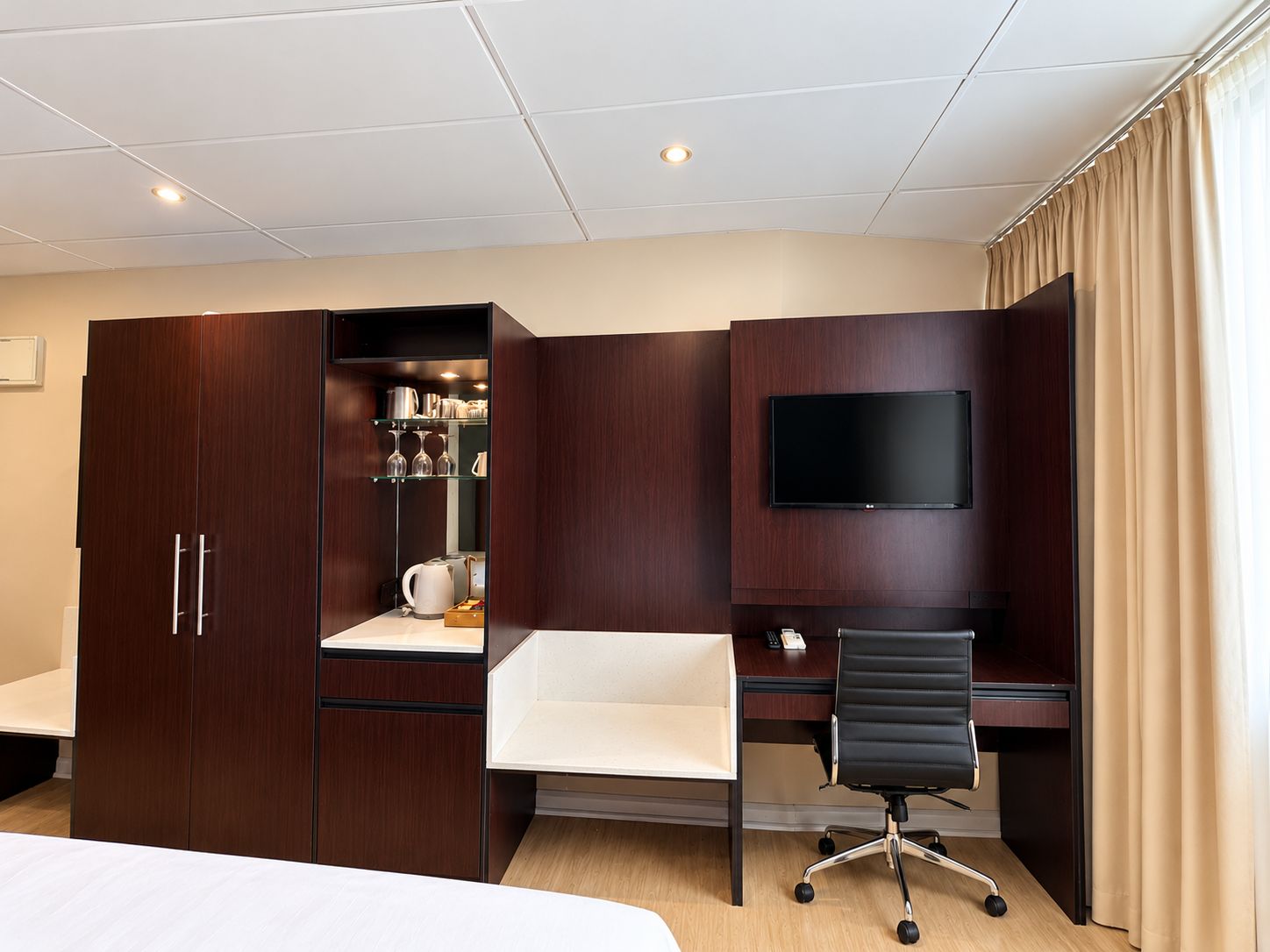A hotel room with a bed, a desk, a chair, a TV, and a wardrobe.