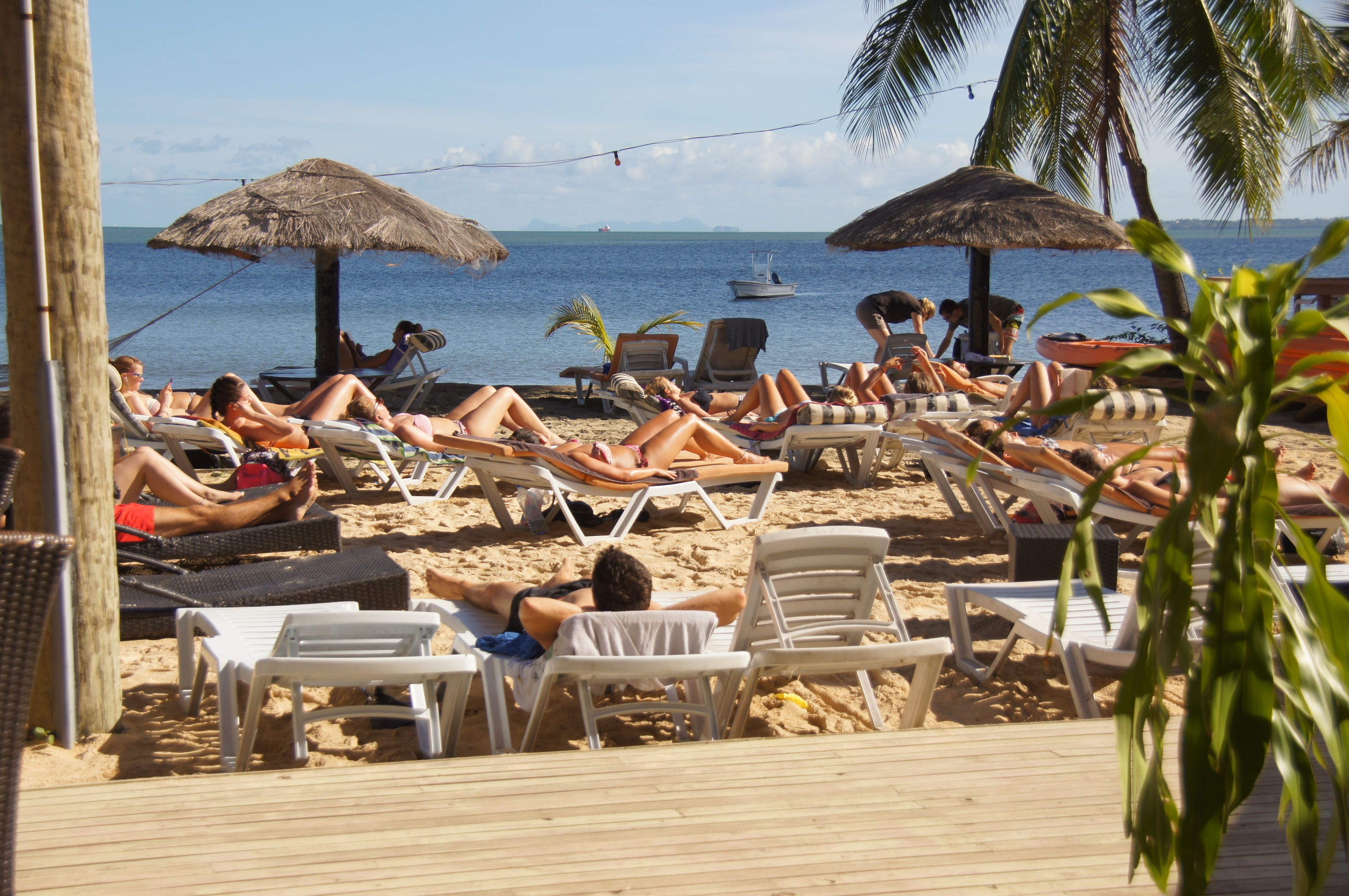 Una playa con sillas de descanso y sombrillas, una terraza de madera y vista al océano.