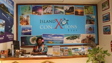 A reception desk at Island X Con-Xions Fiji with a large display of travel posters and a woman behind the counter.