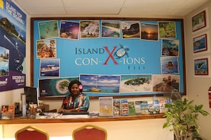 Een receptiebalie bij Island X Con-Xions Fiji, met een grote presentatie van reisposters en een vrouw achter de balie.