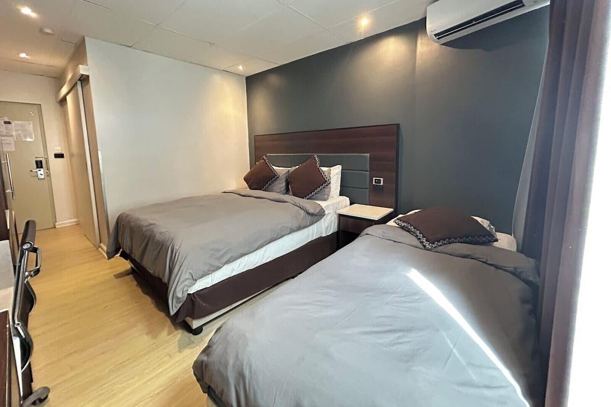 Habitación de hotel con dos camas, piso de madera, unidad de aire acondicionado y una puerta con manija.