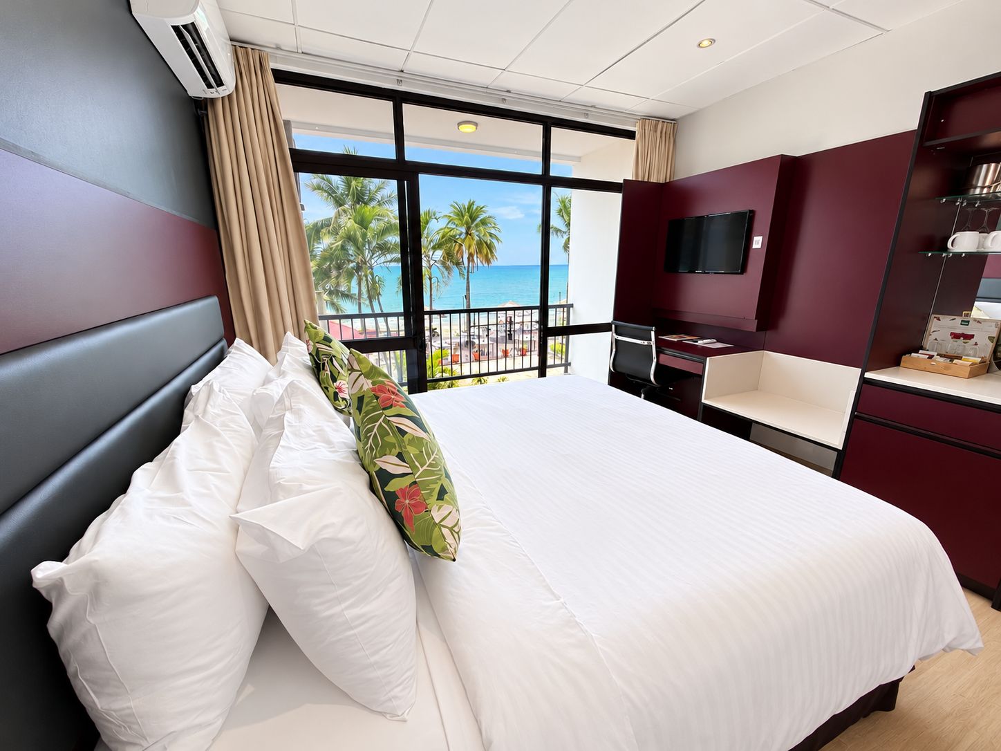 A hotel room with a bed, a desk, a TV, and a view of the beach.