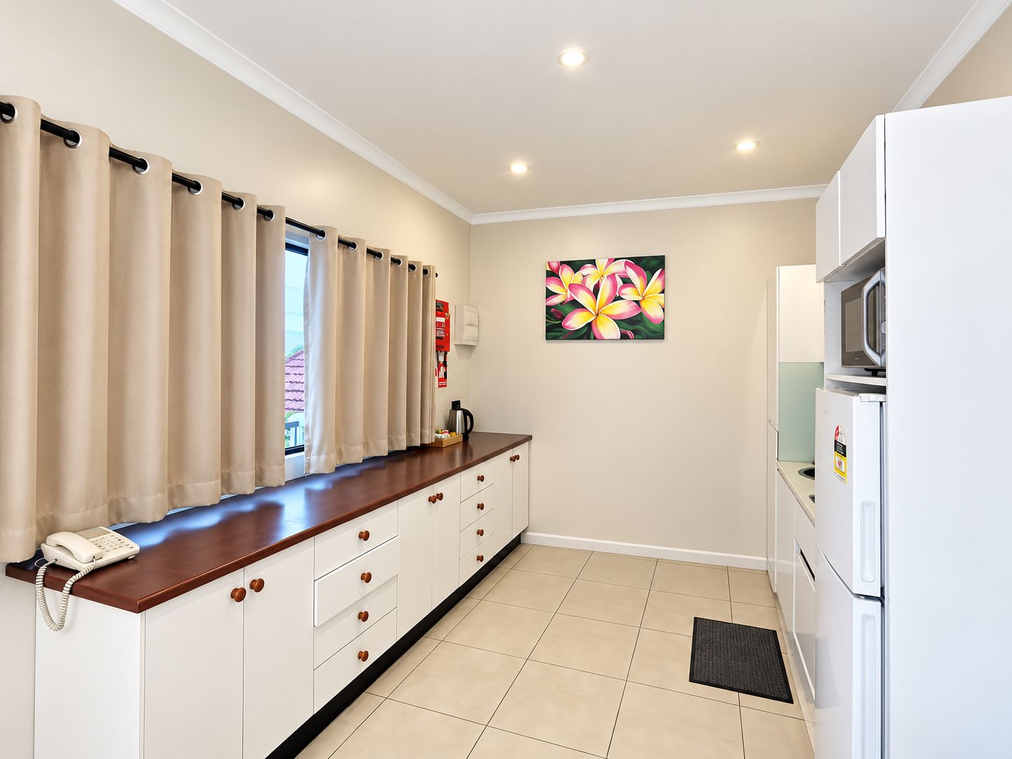 A kitchenette with a wooden countertop, white cabinets, a microwave, and a refrigerator.