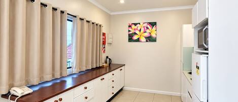 A kitchenette with a wooden countertop, white cabinets, a microwave, and a refrigerator.
