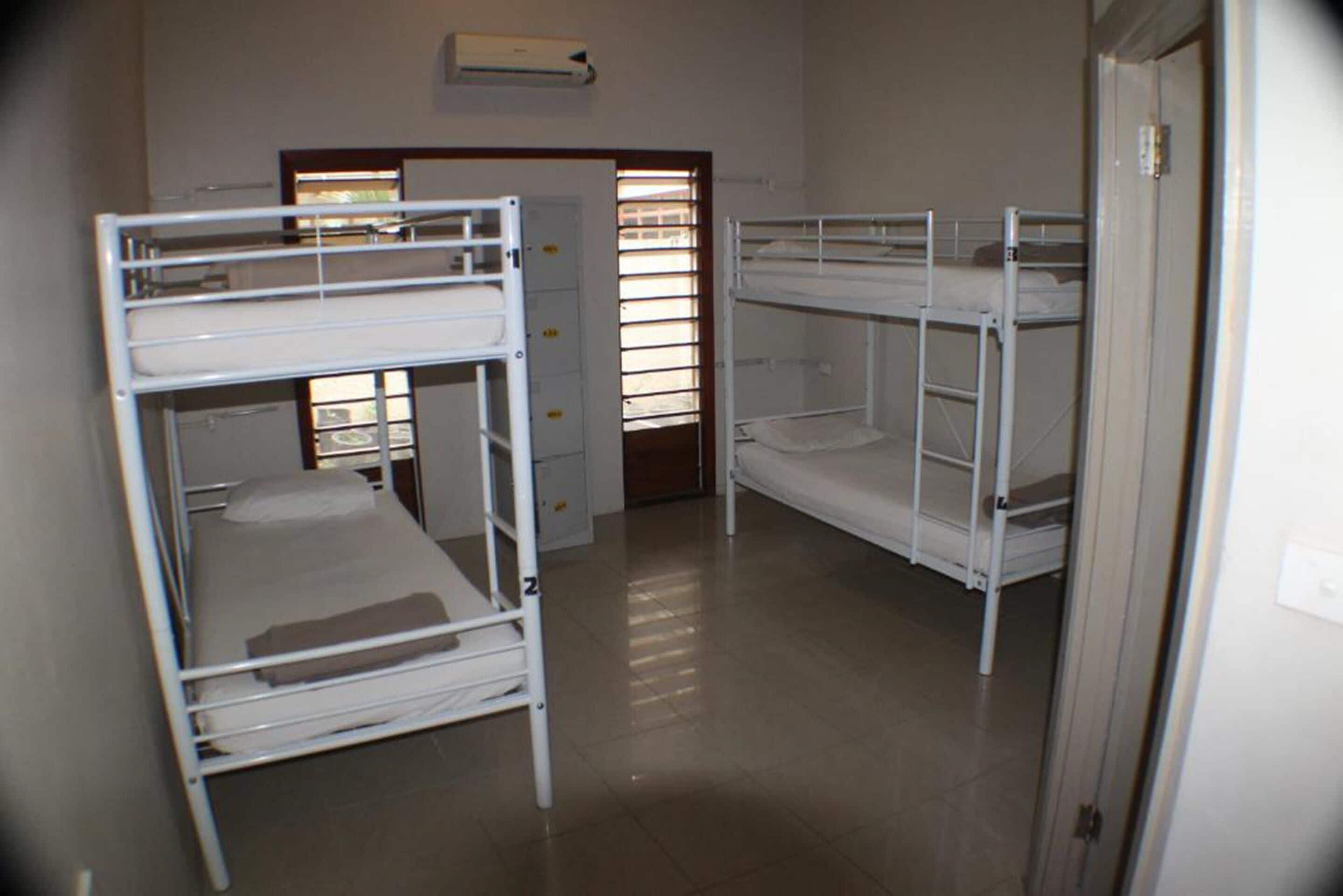 Une chambre de dortoir avec des lits superposés, une porte et une fenêtre avec des stores.