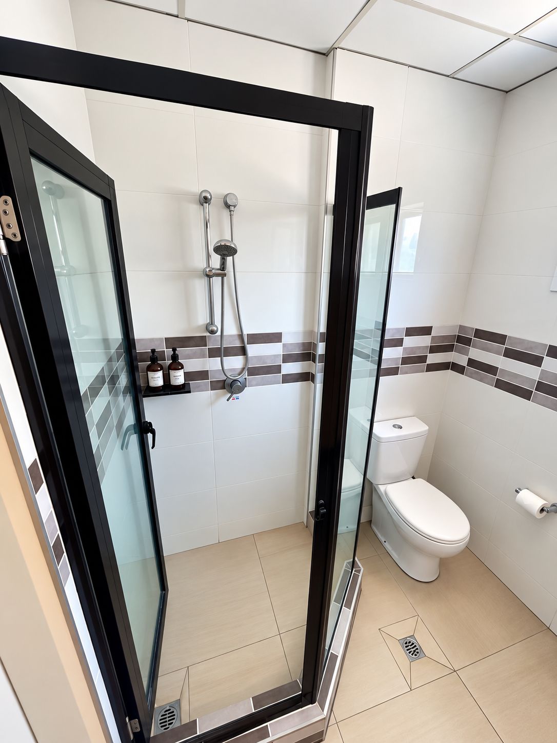 A modern bathroom with a glass-enclosed shower, a toilet, and a sink with toiletries.