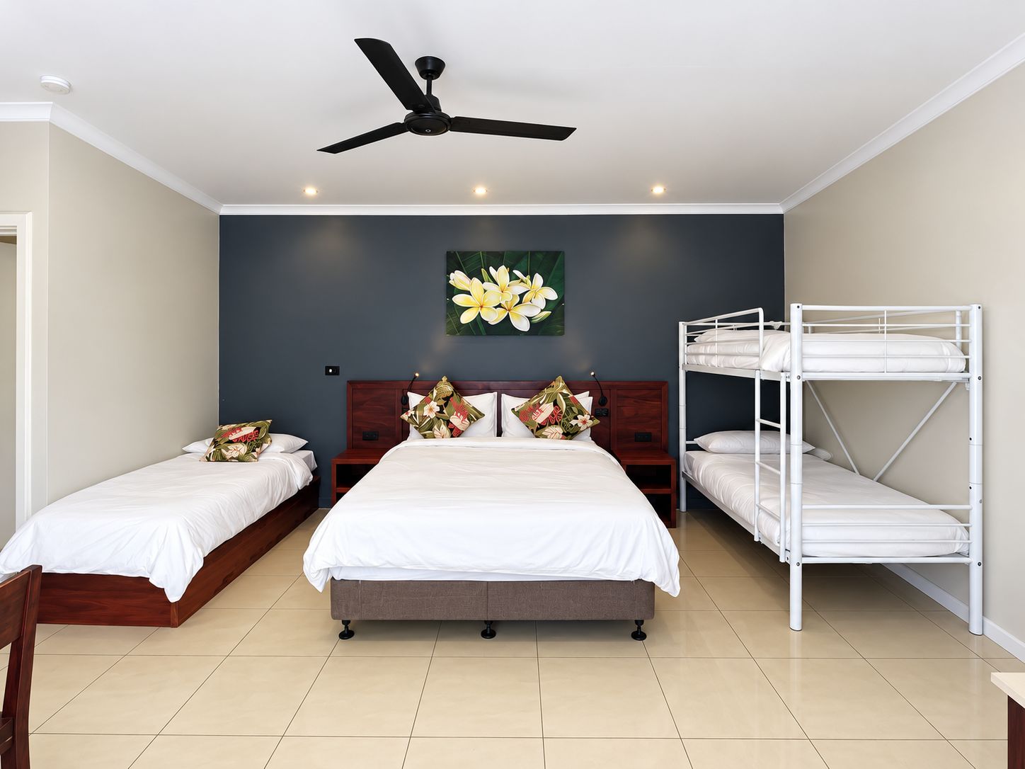 A hotel room with a large bed, two smaller beds, a ceiling fan, and a bunk bed.