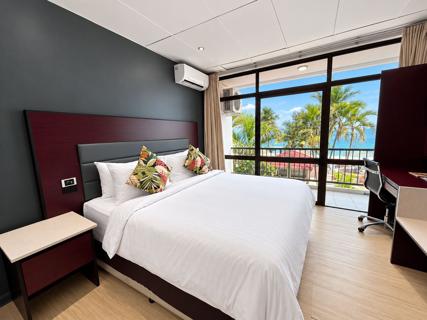 Ein modernes Hotelzimmer mit einem großen Bett, einem Schreibtisch und Blick auf Palmen und das Meer.