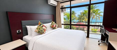 Ein modernes Hotelzimmer mit einem großen Bett, einem Schreibtisch und Blick auf Palmen und das Meer.