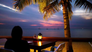 Relax under the shade of a palm tree with a table and chairs overlooking the ocean.