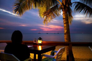 A person sitting at a table with a view of the ocean and sailboats at sunset. - Smugglers Cove Beach Resort and Hotel (Nadi)