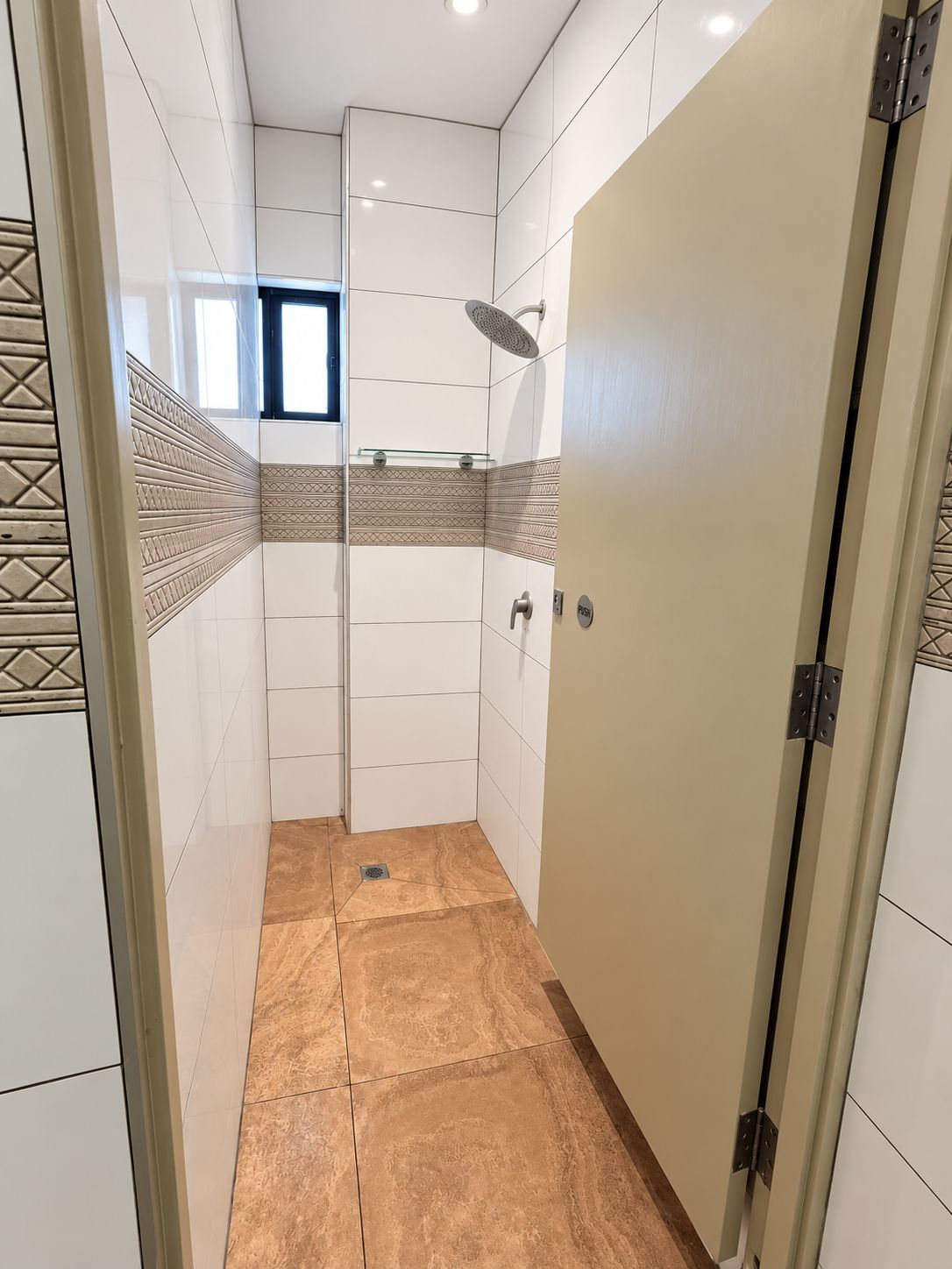 Un baño con ducha, puerta de vidrio y azulejos estampados.