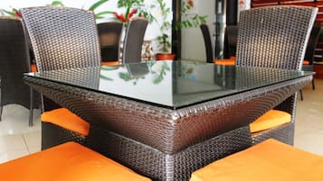Una mesa de comedor con cubierta de vidrio, rodeada de sillas de mimbre con cojines naranja.