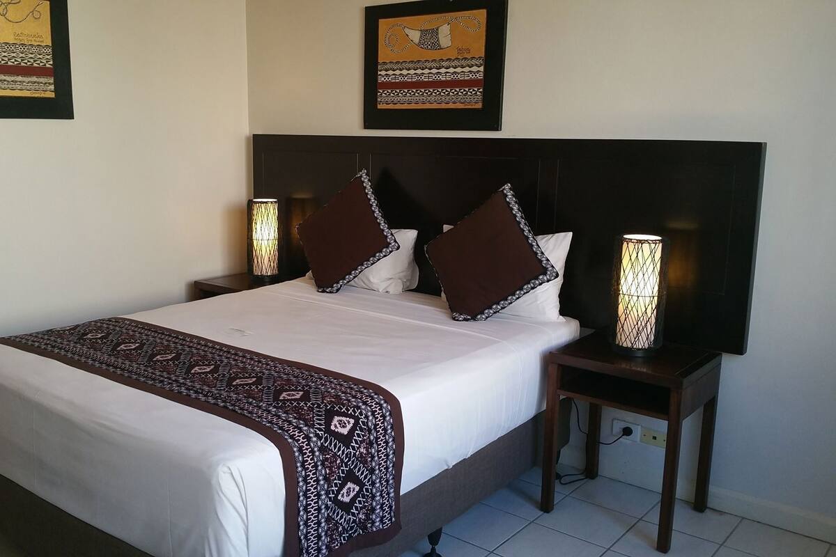 Una cama bien hecha con una colcha estampada, dos lámparas de noche y un cabecero.