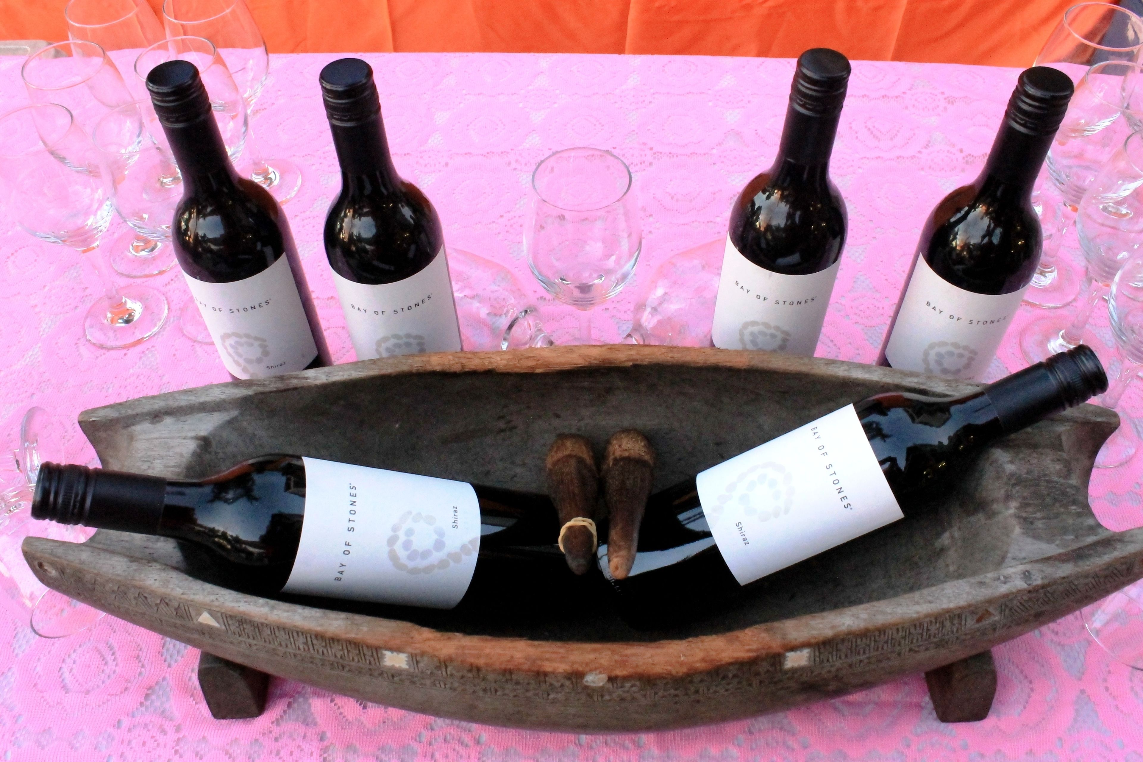 Una botellera de madera con varias botellas de vino con etiquetas, sobre una mesa con mantel rosa.