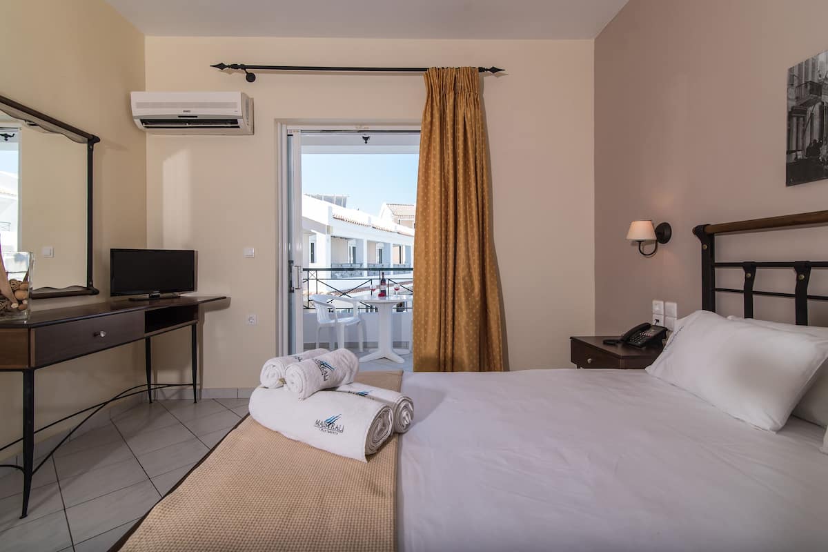 Een hotelkamer met een bed, een bureau met een televisie, een balkon met een tafel en stoelen, en een raam met gordijnen.