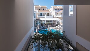 Une vue d’une zone de piscine avec des chaises longues et des parasols, entourée d’immeubles dotés de balcons.