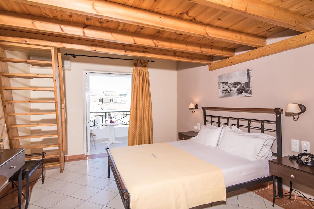 Een slaapkamer met een bed, houten balken in het plafond, een bureau en een raam met gordijnen.