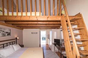A bedroom with a wooden ceiling, a bed, a desk, and a TV.