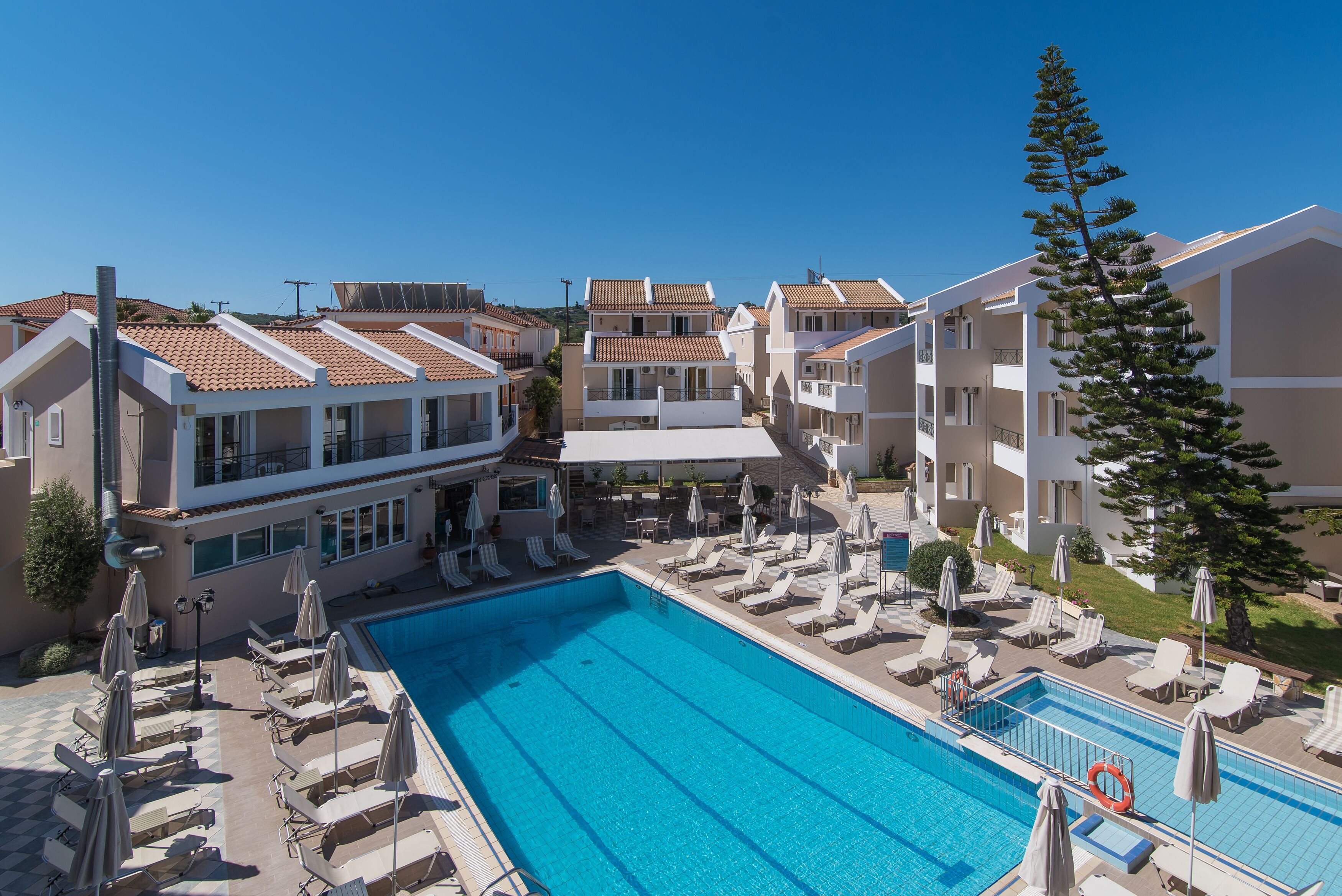 A swimming pool with lounge chairs and umbrellas, surrounded by multi-story buildings with balconies.