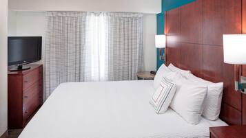 A hotel room with a large bed, a television on a wooden dresser, a nightstand with a lamp, and a window with curtains.
