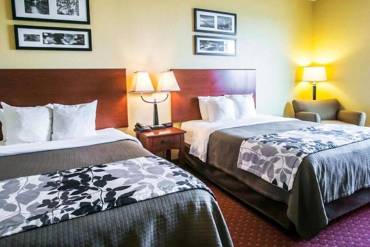 A hotel room with two beds, a wooden headboard, a nightstand with a lamp, and framed pictures on the wall.