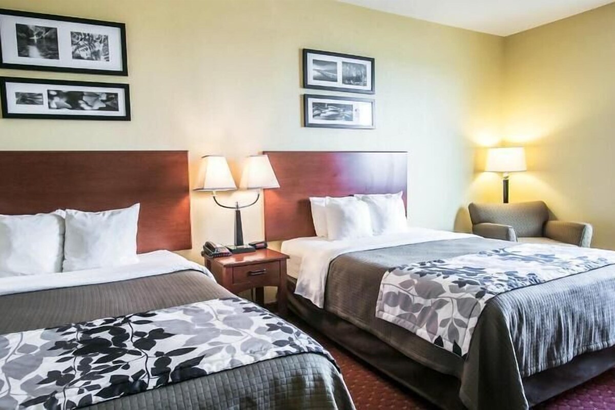 A hotel room with two beds, a nightstand, a chair, and three framed pictures on the wall.