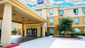 A hotel entrance with a sign reading "Sleep Inn & Suites," featuring a covered entrance, a red carpet, and a landscaped area with a tree. - Sleep Inn & Suites New Braunfels (New Braunfels)