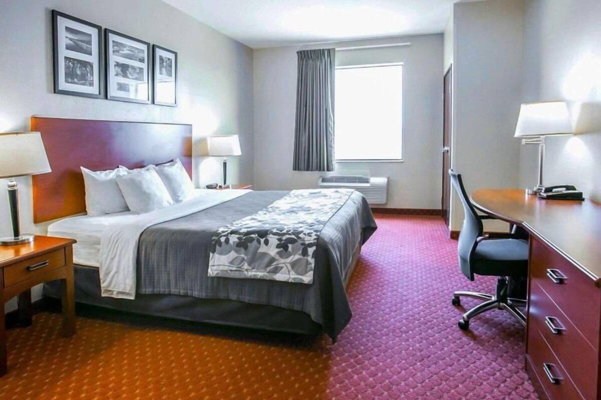 A hotel room with a large bed, a desk, a chair, and a window with curtains.