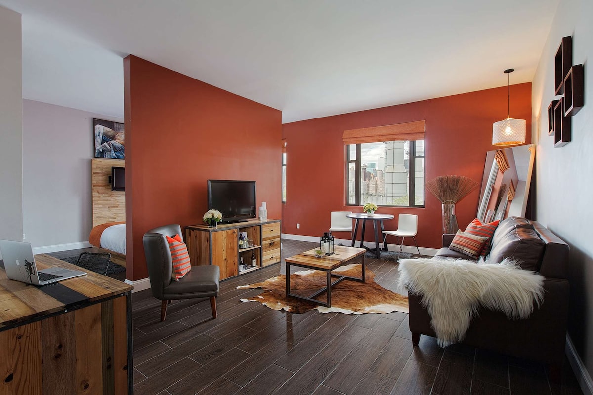 Een moderne woonkamer met een rode accentmuur, een leren bank, een salontafel, een televisie, en een eetgedeelte met een witte stoel en tafel.