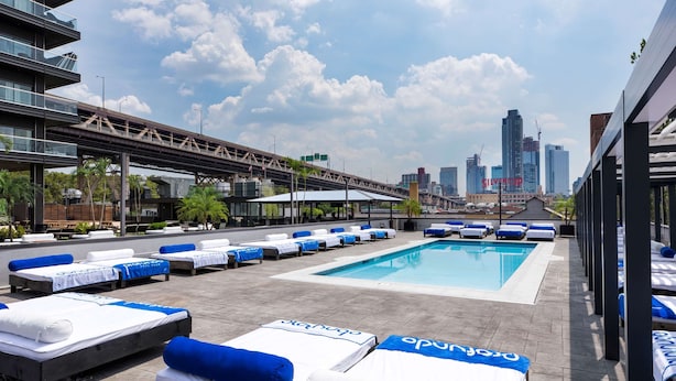 A rooftop pool area with lounge chairs and a view of the city skyline.