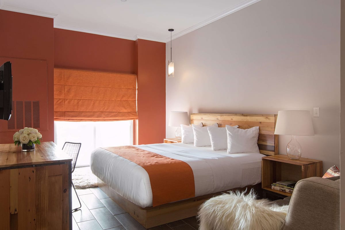 Een slaapkamer met een groot bed, een houten hoofdbord, twee nachtkastjes met lampen, een bureau met een stoel en een raam met luxaflex.