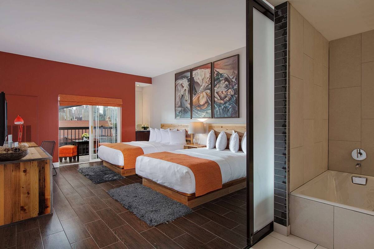 Hotelkamer met twee bedden, een bureau, een stoel, een raam met uitzicht, een schilderij aan de muur en een bad.