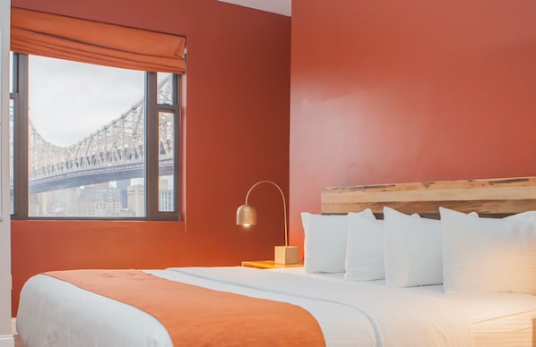 Habitación de hotel con una cama grande, una mesita de noche con una lámpara y vista a un puente por la ventana.
