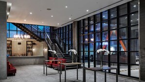 A spacious lobby with a staircase, seating area, and large windows offering views of the city.