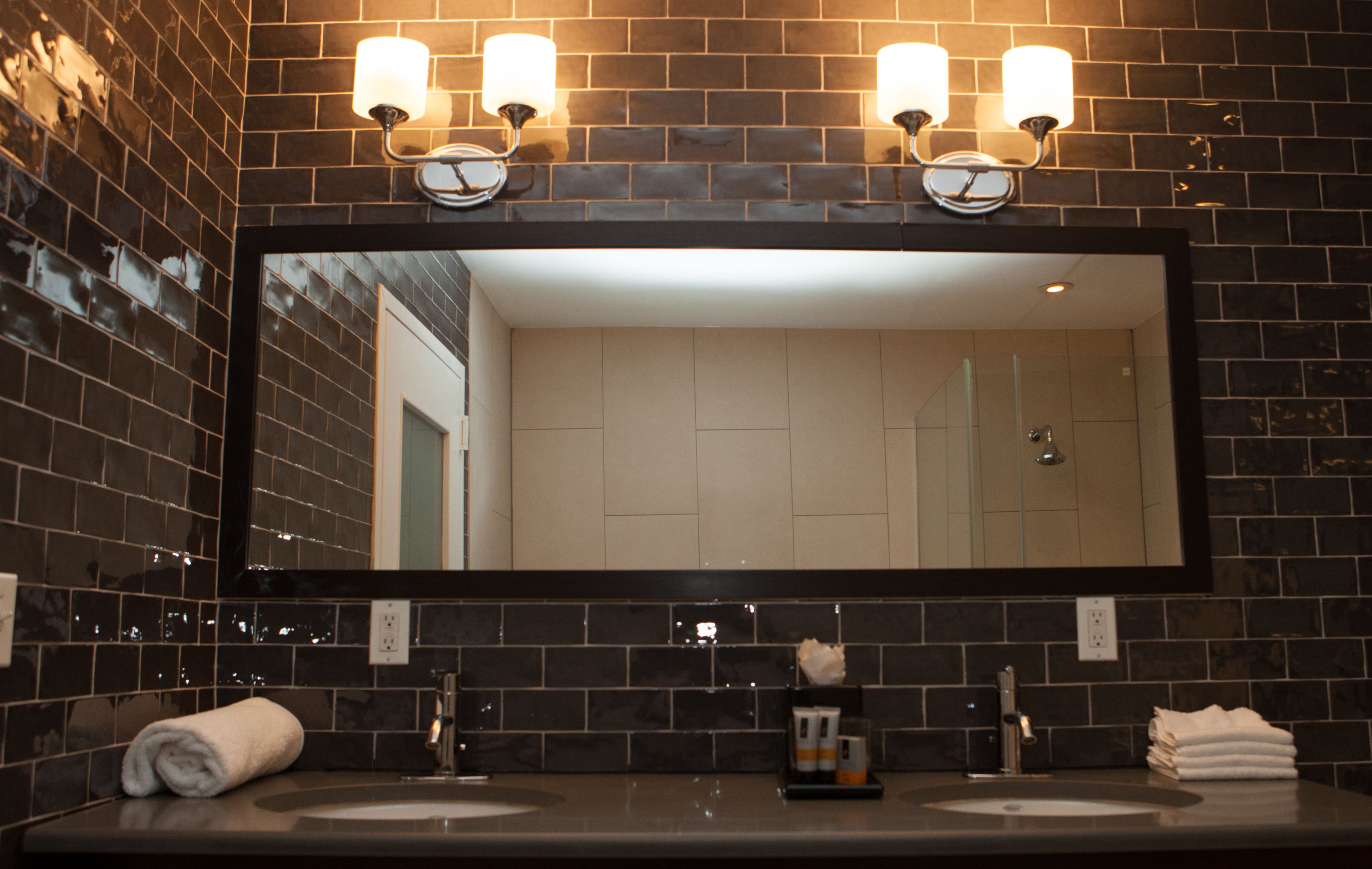 A bathroom with a large mirror, two sinks, and three wall-mounted lights.