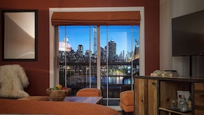 A hotel room with a large window offering a city view, a bed, a seating area with a table, and a TV on a wooden cabinet.