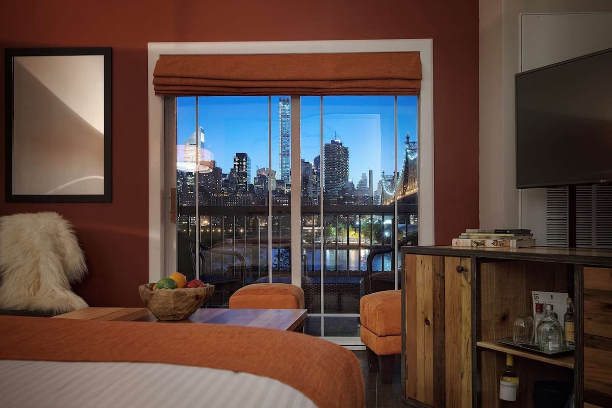 Hotelkamer met een groot raam met uitzicht op de stad, een bed, een zithoek met een tafel en een televisie op een houten kast.