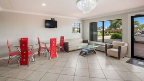 A modern living room with a glass coffee table, red chairs, a beige sofa, and a television mounted on the wall. - Econo Lodge Lake Charles University Area (Lake Charles)