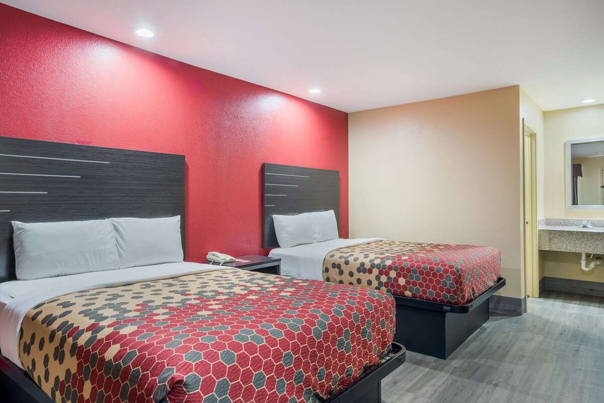 Een hotelkamer met twee bedden, elk voorzien van een beddekleed met dessin, een nachtkastje met telefoon en een vastgezet hoofdbord.