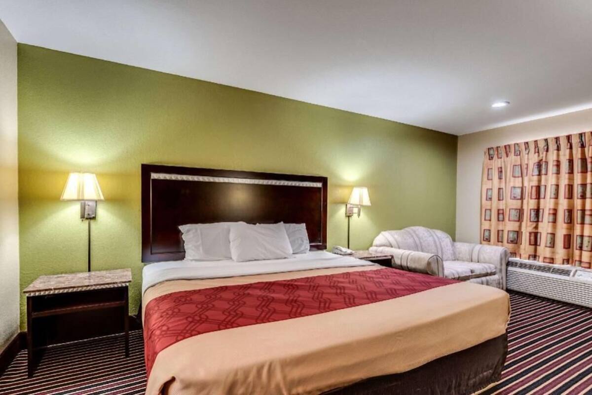 Een hotelkamer met een bed, twee bedlampen, een stoel, een kachel en een kamerbreed tapijt met een patroon.