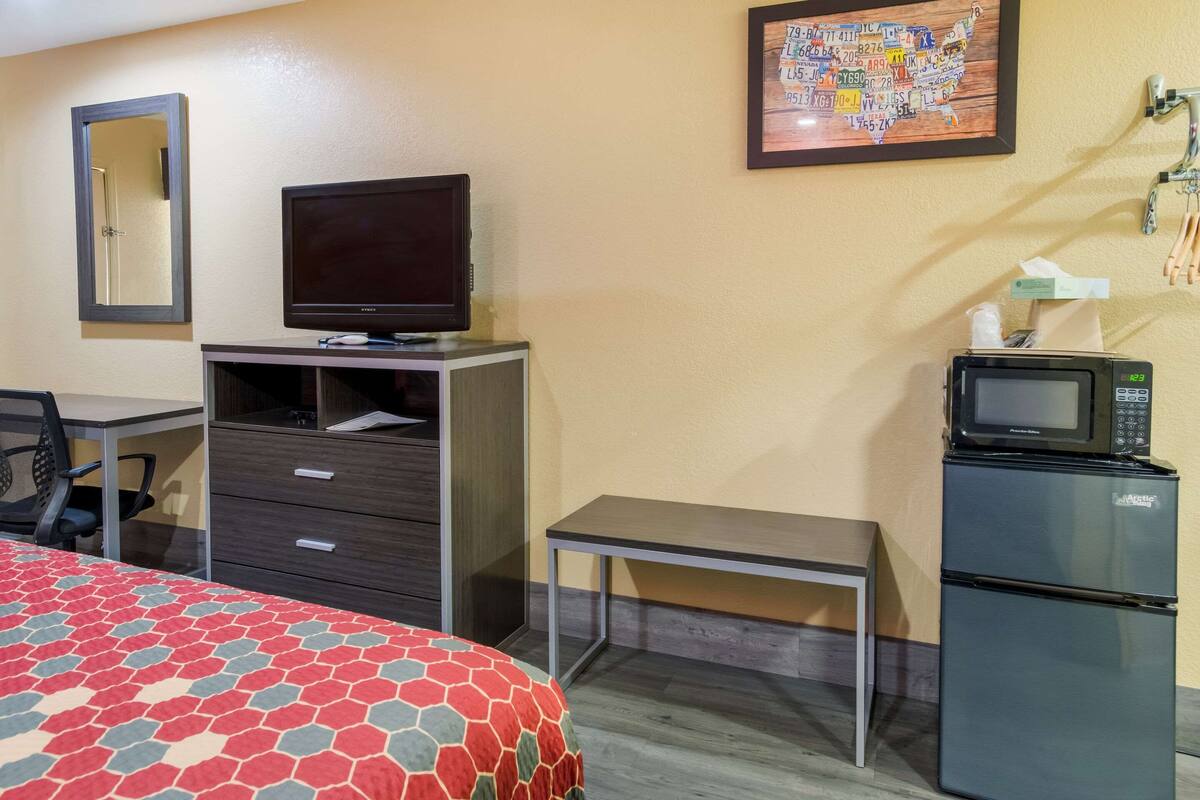 Een hotelkamer met een bed, een bureau, een televisie, een koelkast en een magnetron.