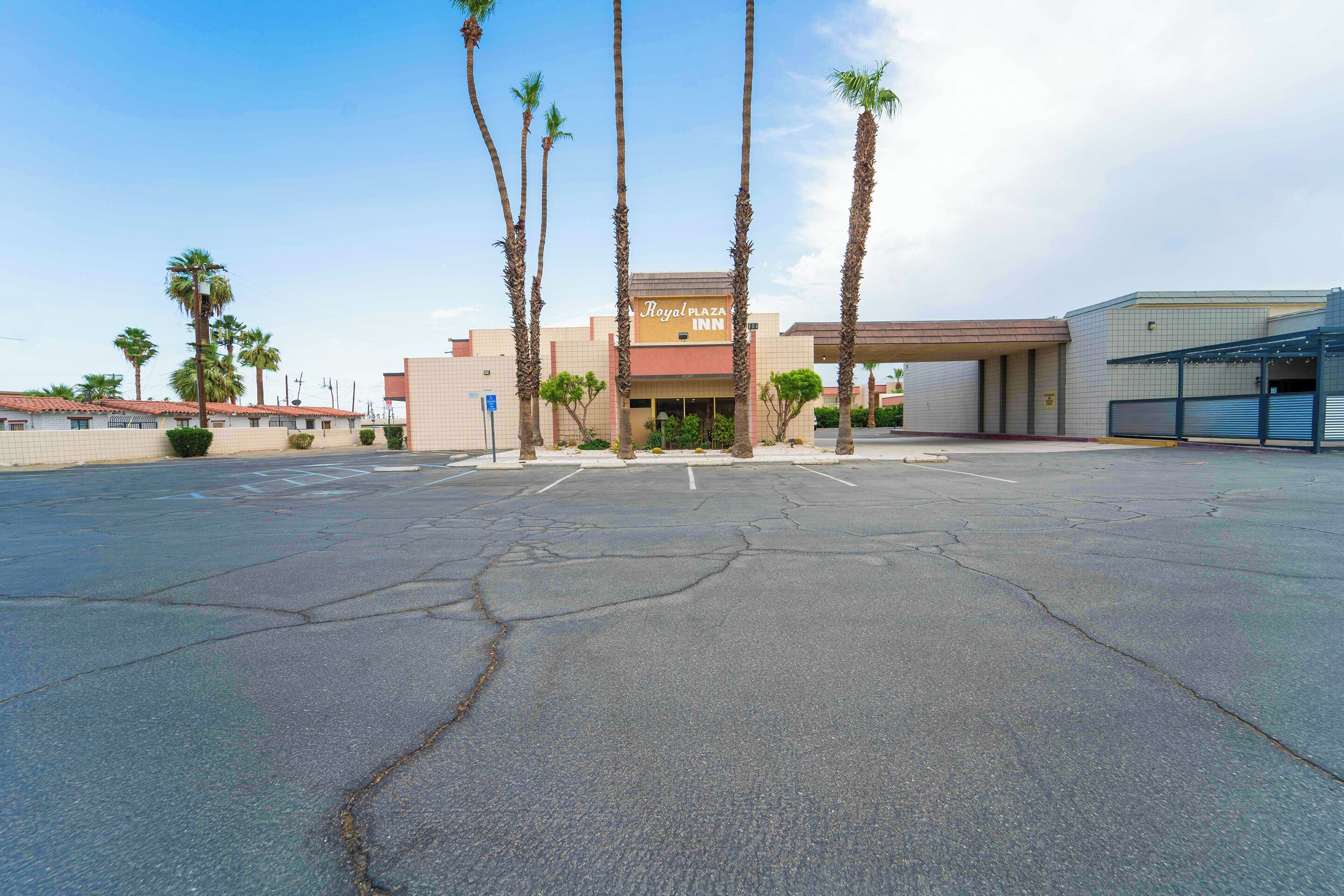 A Royal Plaza Inn with a parking lot, palm trees, and a building with a tiled facade.