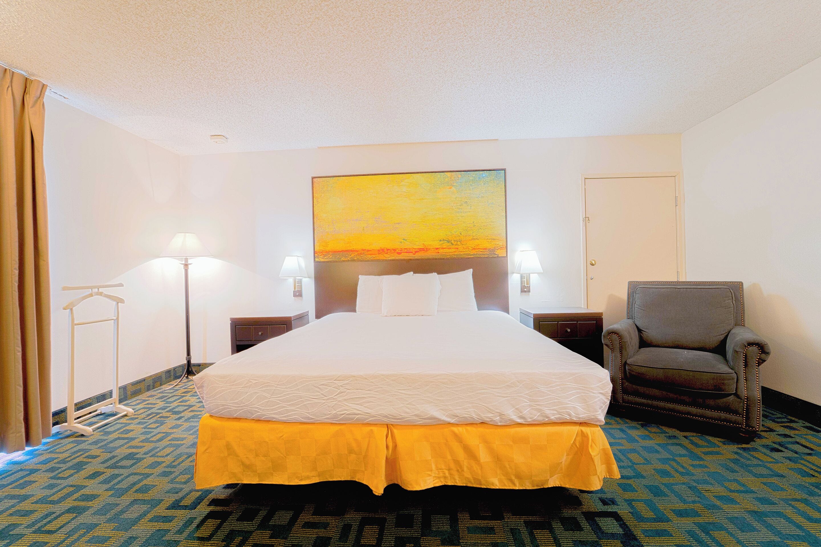 Una camera d'albergo con un letto, una sedia, un quadro e una lampada.