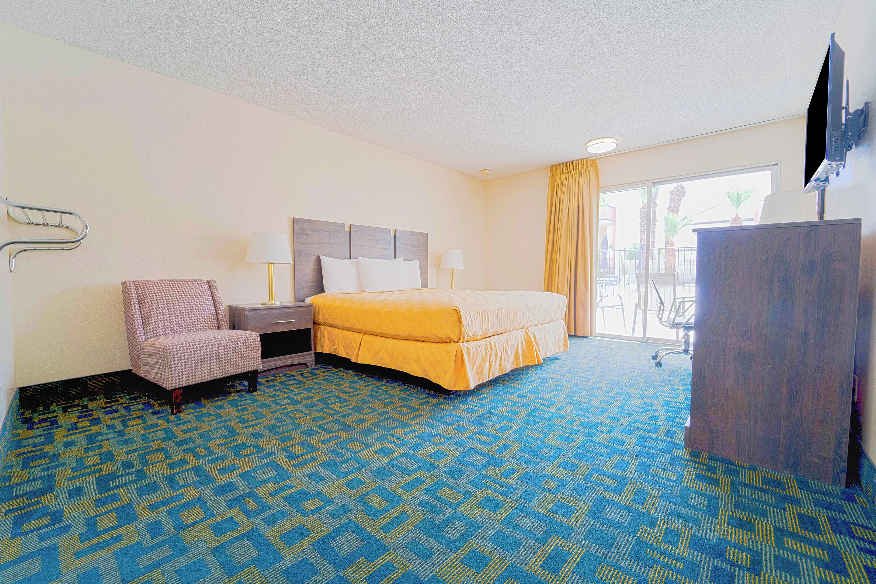 Ein Hotelzimmer mit Bett, Schreibtisch, Stuhl, Fernseher und Blick ins Freie.