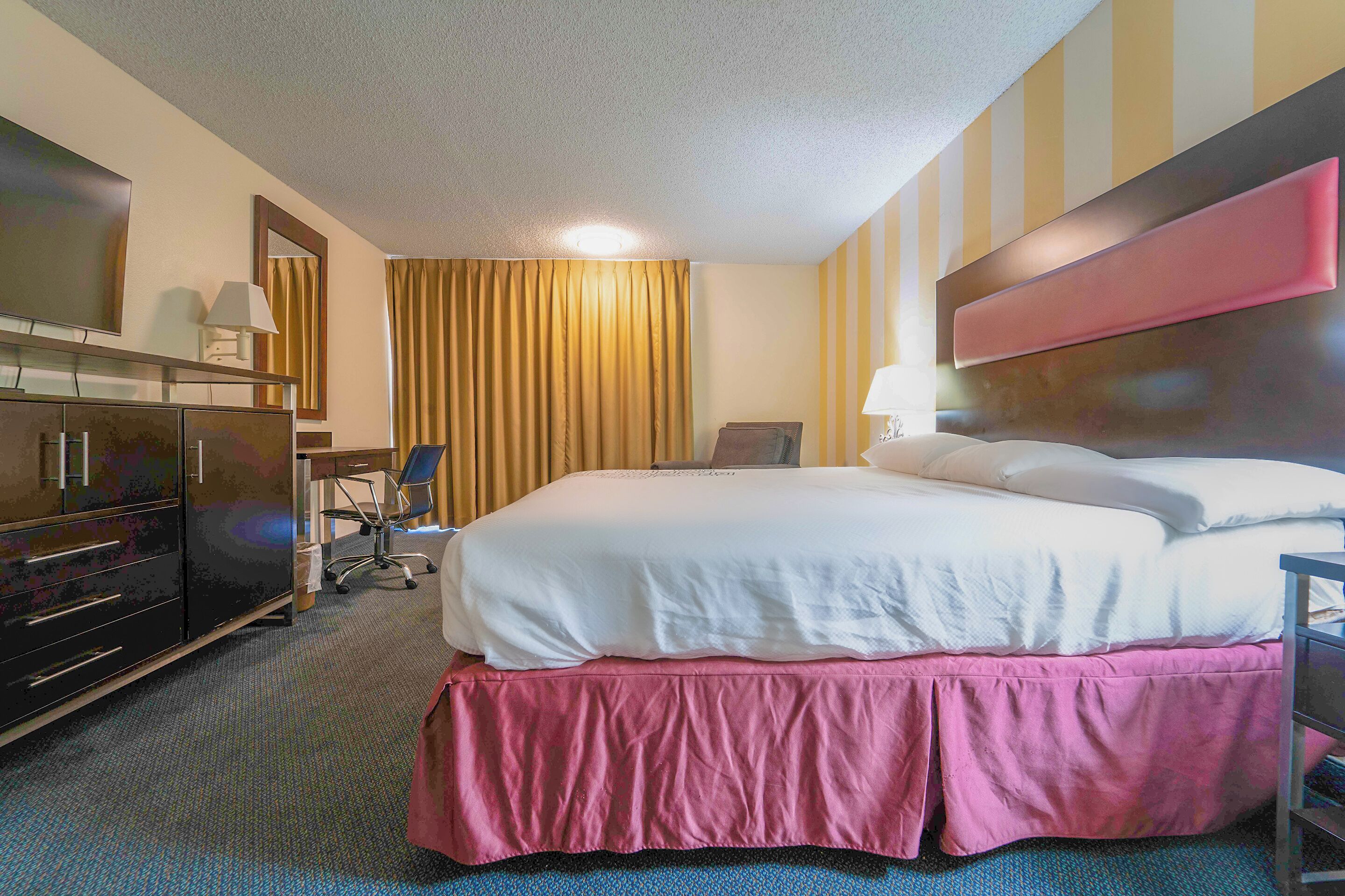 Ein Hotelzimmer mit einem großen Bett, einem Schreibtisch, einem Sessel, einem Fernseher und einem Kleiderschrank.