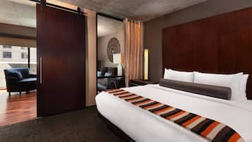 A hotel room with a large bed, a wooden headboard, a desk with a chair, a sofa, and a view of the outside.
