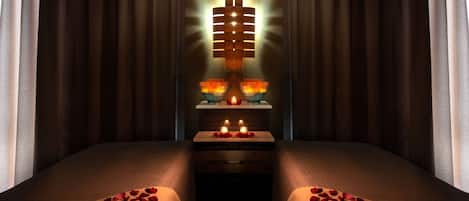 A hotel room with two beds, a bedside table with candles, and a wall-mounted light fixture.